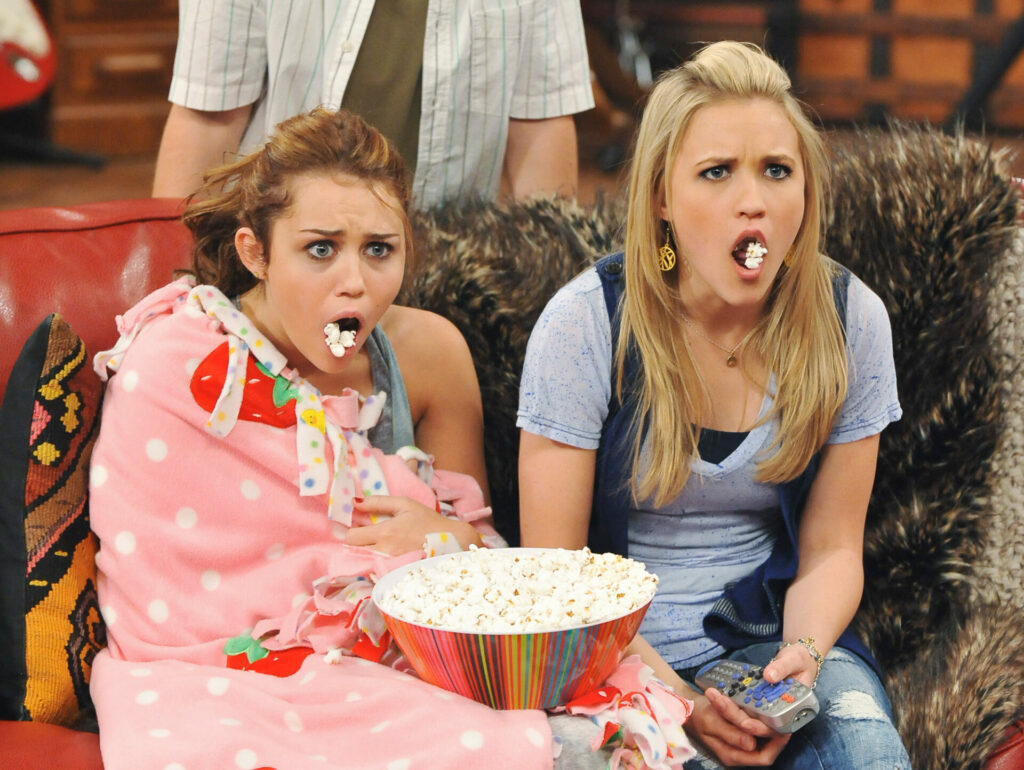 Passion of Arts: Miley und Lilly schauen mit offenen Mündern und Popcorn darin entsetzt in den Fernseher