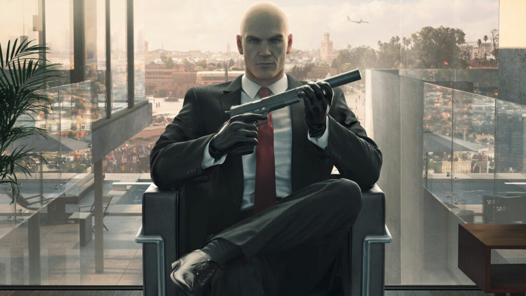 Passion of Arts: Der Hitman sitzt auf einem Stuhl vor einer großen Glasfront, hinter ihm ein Panorama einer Stadt und hält seine Waffe in der Hand | Fragen zu Brettspielen und Video Games