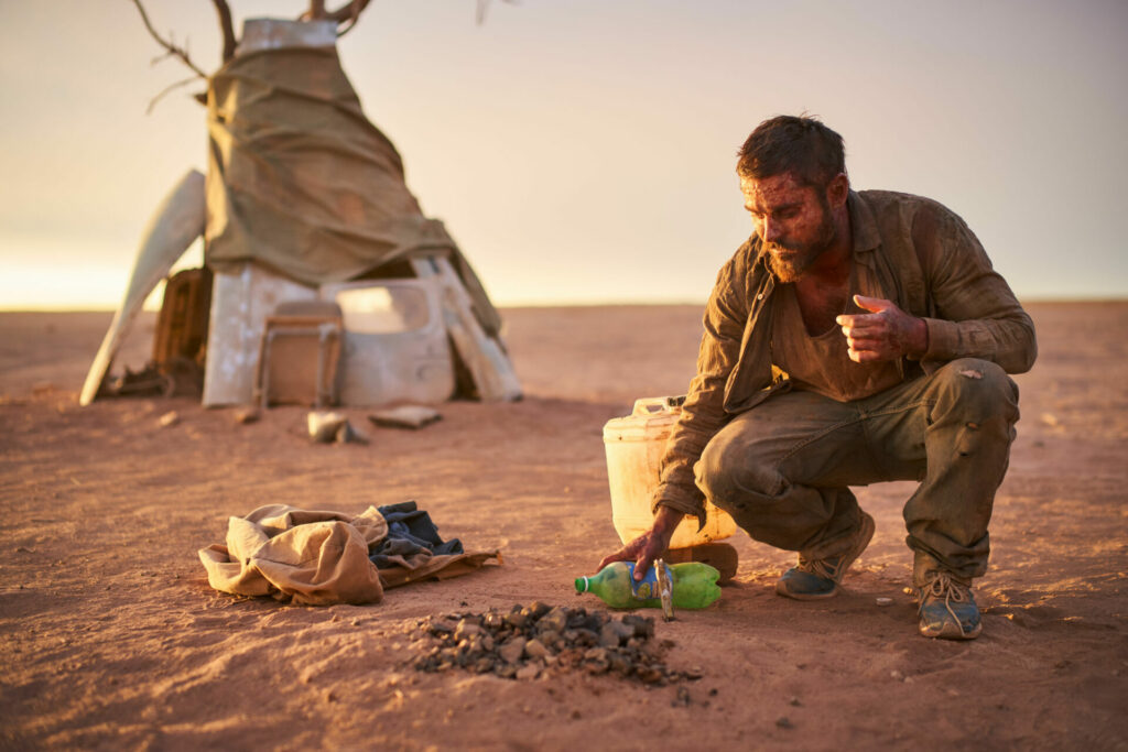 Passion of Arts: Zac Efron kniet in der Wüste und gießt etwas Wasser auf die Feuerstelle um sie zu löschen