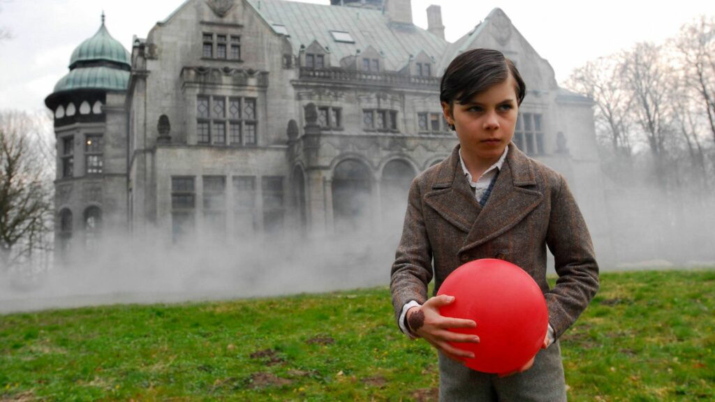 Passion of Arts: Gonger steht vor einem düsteren Haus, hält einen roten Ball in der Hand und schaut grimmig