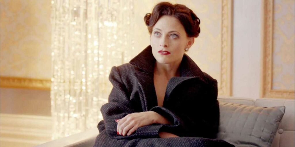 Passion of Arts: Irene Adler sitzt auf einem Sofa und trägt nichts außer Sherlocks Mantel