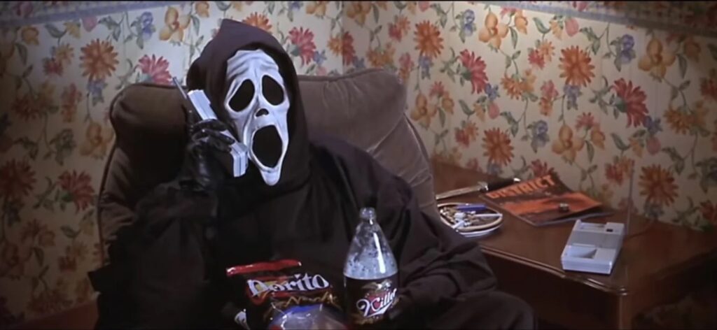 Passion of Arts Scary Movie: Der Mann mit der Maske sitzt in einem Sessel. Auf seinem Schoß ist eine Killer Coke und Dorito Chips. Er hält eine Telefon in der Hand. Neben ihm auf dem Tisch steht ein Aschenbecher, liegt ein Messer und die Zeitschrift District