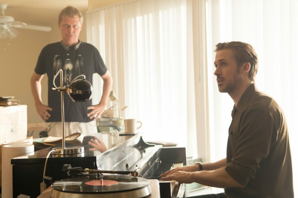 Ryan Gosling sitzt rechts am Klavier und hört jemandem zu, der ihm Anweisungen gibt. La La Land