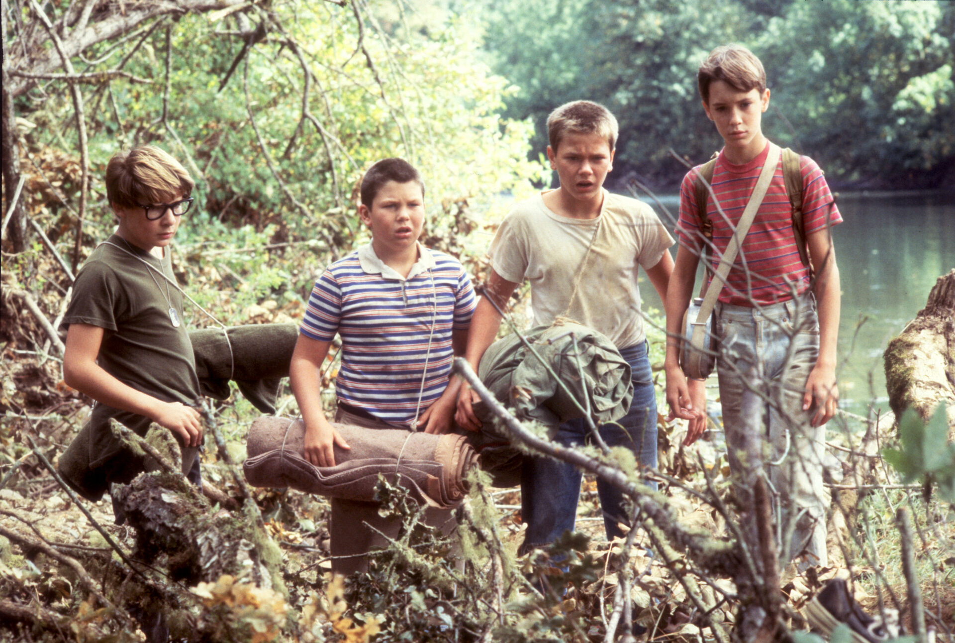Die 5 besten filmischen Sommerabenteuer: die vier Jungs stehen mit Sack und Pack im Wald und schauen entsetzt auf etwas im Dickicht. Hinter ihnen sieht man einen See | Die 5 besten Filme im Grünen
