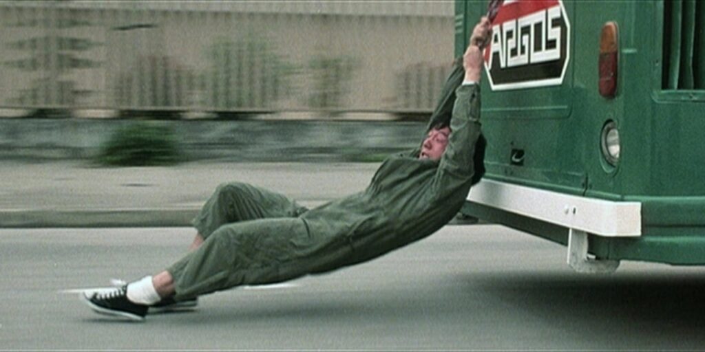 Stunts im Film: Jackie Chan hängt am Heck eines Lasters. Seine Füße schleifen dabei über den Boden