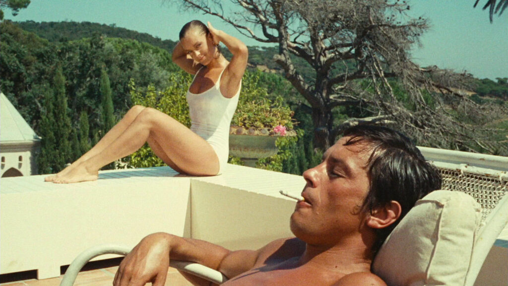 Die 5 besten sommerlichen Gebiete in Filmen: Romy Schneider sitzt auf der Brüstung und hält sich die Haare hinter den Kopf. Alain Delon sitzt weiter vorn im Liegestuhl, raucht eine Zigarette und hat die Augen geschlossen
