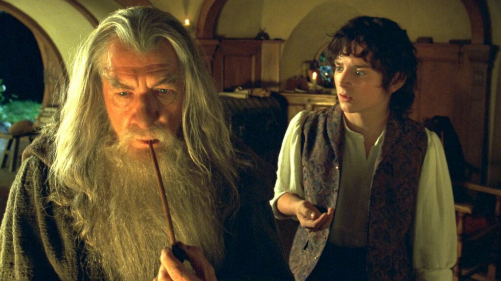 Epische Fantasy-Filme: Links sitzt Gandalf und zieht nachdenklich an seiner Pfeife. Rechts steht Frodo mit dem Ring in der Hand und schaut entsetzt auf Gandalf, da er ihm gerade die Geschichte des Ringes erzählt hat