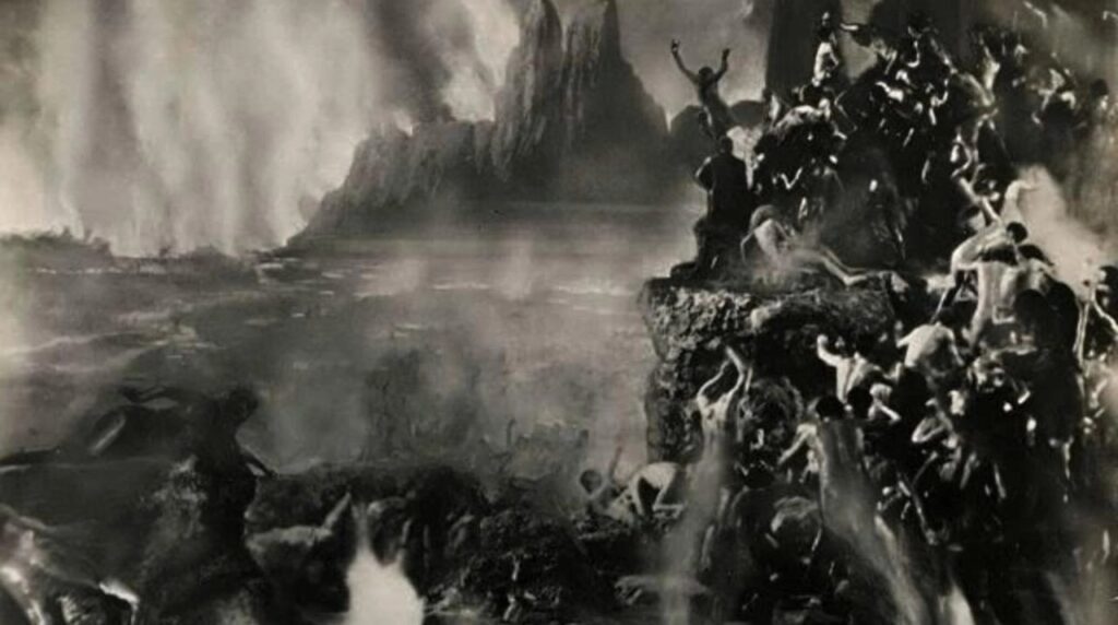 Horror im Film: Das Bild Zeigt auf der rechten Seite viele Menschen, die einen Berg erklimmen und vor dem Feuer, das unten brennt, fliehen. Im Hintergrund ist ein weiterer Berg und das Feld, das sich dort hin erstreckt steht in Flammen