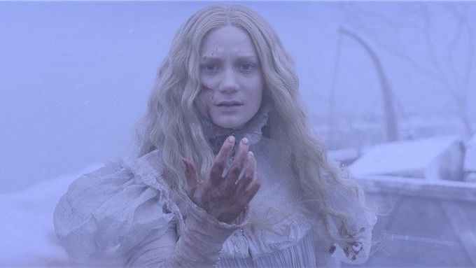 Die 5 besten Lieblings-Horrorfilm Charaktere: Edith steht draußen im Schnee. Um sie herum ist alles lila und weiß. Sie selbst wirkt auch eher wie ein Geist. Sie hat Blut im Gesicht und an der Hand. Die Hand hält sie nach oben etwas vor ihr Gesicht