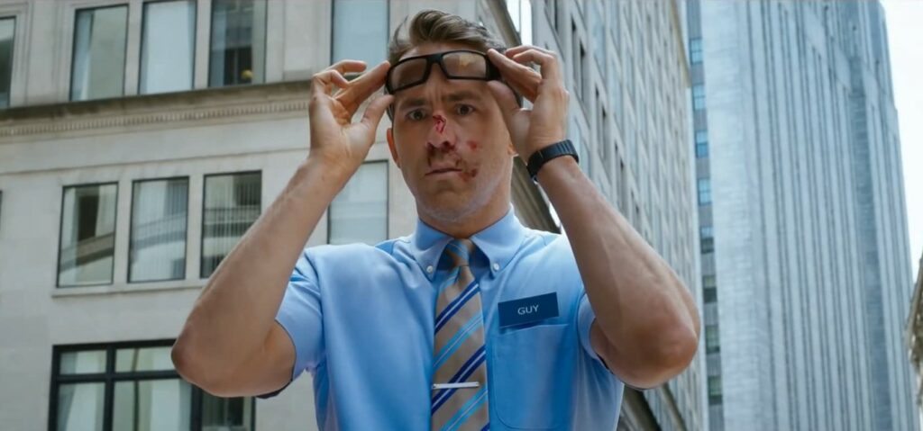 Die 5 besten Science-Fiction-Filme der letzten Dekade: Free Guy steht vor einem Wolkenkratzer. Er trägt ein hellblaues Hemd, eine gestreifte Krawatte und ein Schild mit der Aufschrift "Guy". Seine Nase blutet, außerdem hält er sich eine Brille an die Stirn