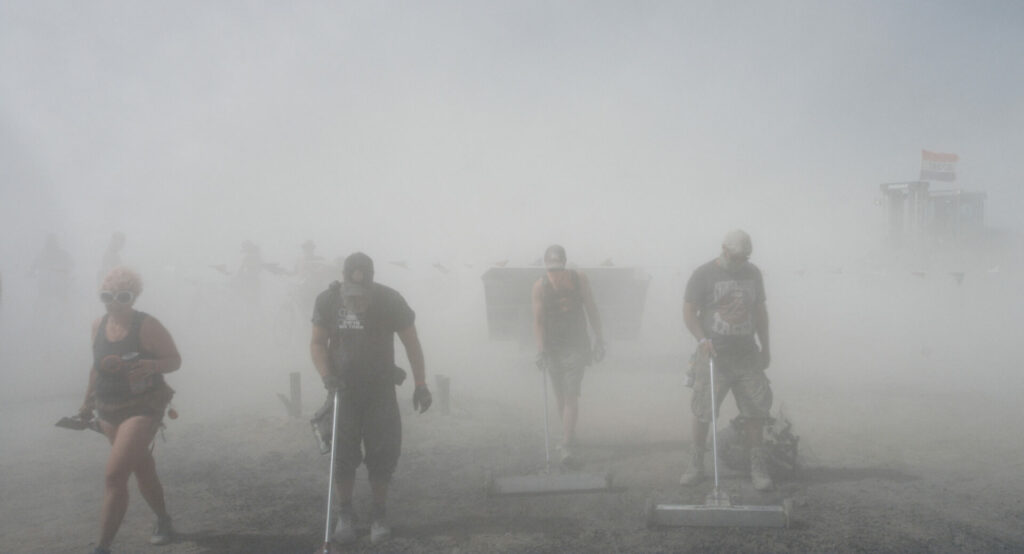 Trash & Heavy Metal: Das Bild zeigt mehrere Menschen, die in einer Staubwolke den Boden mit Metalldetektoren absuchen