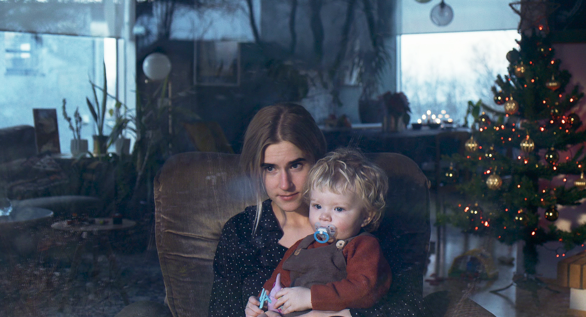 Echo: Auf dem Bild sitzt eine junge Frau in einem Ledersessel. Auf ihrem Schoß ist ein blondes Kind mit einem Schnuller. Im Hintergrund sieht man Fenster, Pflanzen und rechts einen geschmückten Weihnachtsbaum