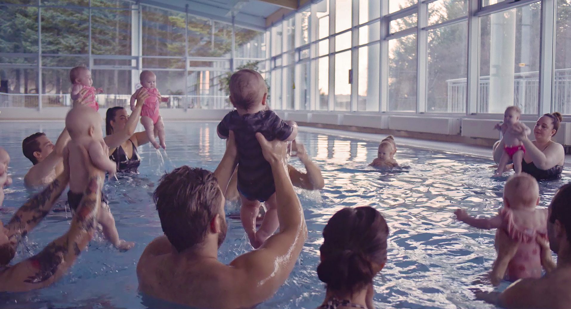 Echo: Auf dem Bild sind Menschen in einem Hallenbad zu sehen, die Babys in ihren Händen halten und diese nach oben aus dem Wasser heben
