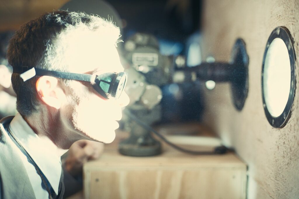 Fragen zu Kinofilmen und Filmen aus dem Jahr 2023: Auf dem Bild schaut ein Mann mit einer Schutzbrille durch ein Bullauge. Daraus strahlt enorm helles Licht