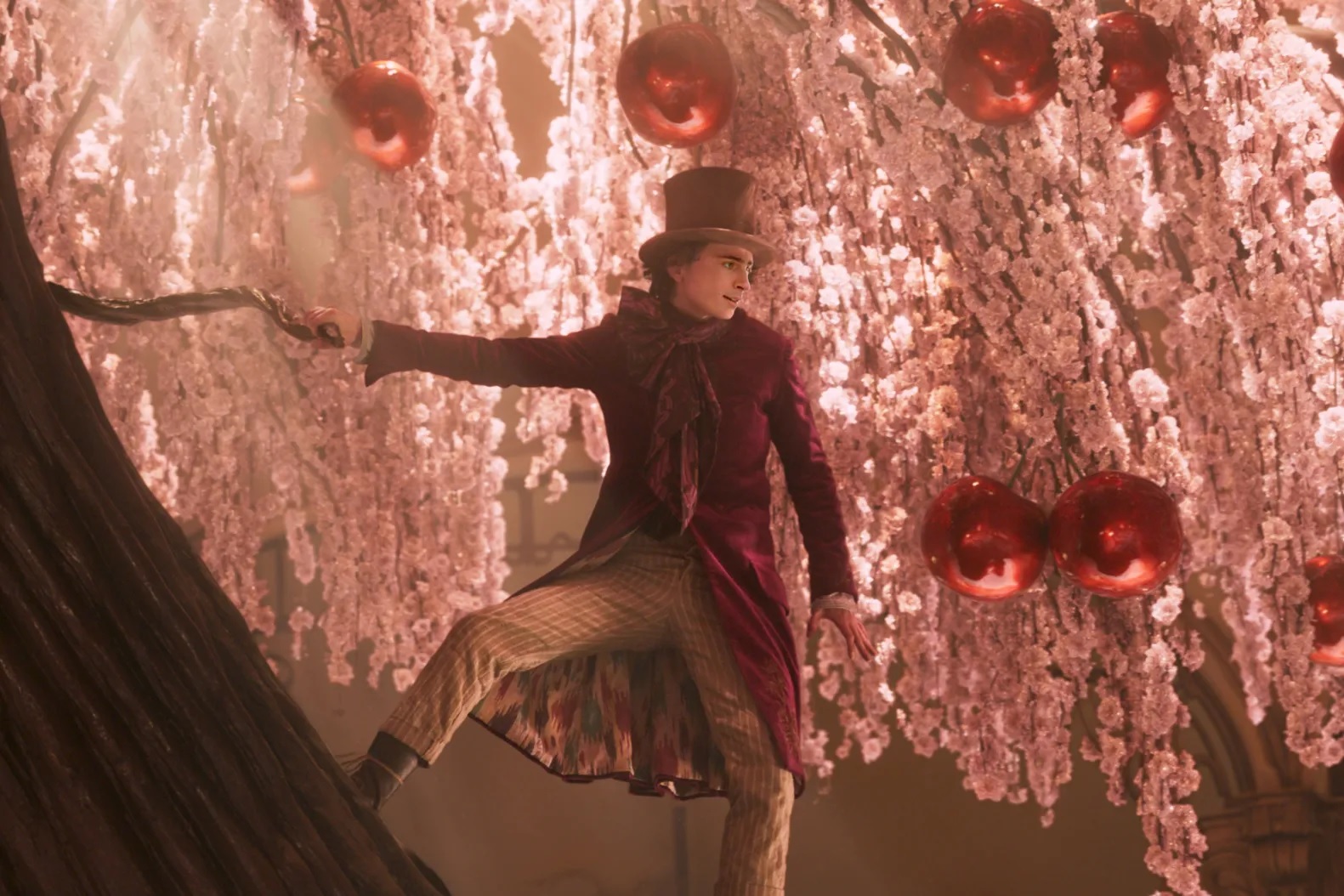 Auf dem Bild sieht man Willy Wonka, der auf einem Schokoladenbaum mit roas Blüten und großen, roten, glänzenden Kirschen steht.