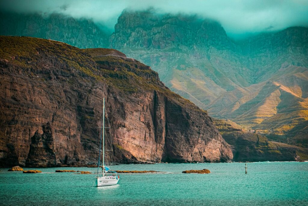 Fragen zu Reisen, Reiseziele und Reiseerfahrungen: Auf dem Bild sieht man viele Felsen und Berge. Vorne im Wasser fährt ein Segelboot