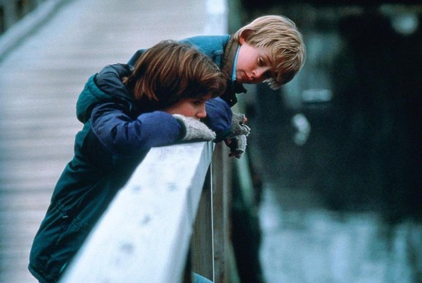 Fragen zu Buchverfilmungen: Das Bild zeigt zwei Jungs, die an einer Brücke stehen. Einer lehnt sich etwas über das Geländer und schaut den anderen Jungen an. Der andere Junge hat die Arme auf dem Geländer verschränkt und blickt nachdenklich drein