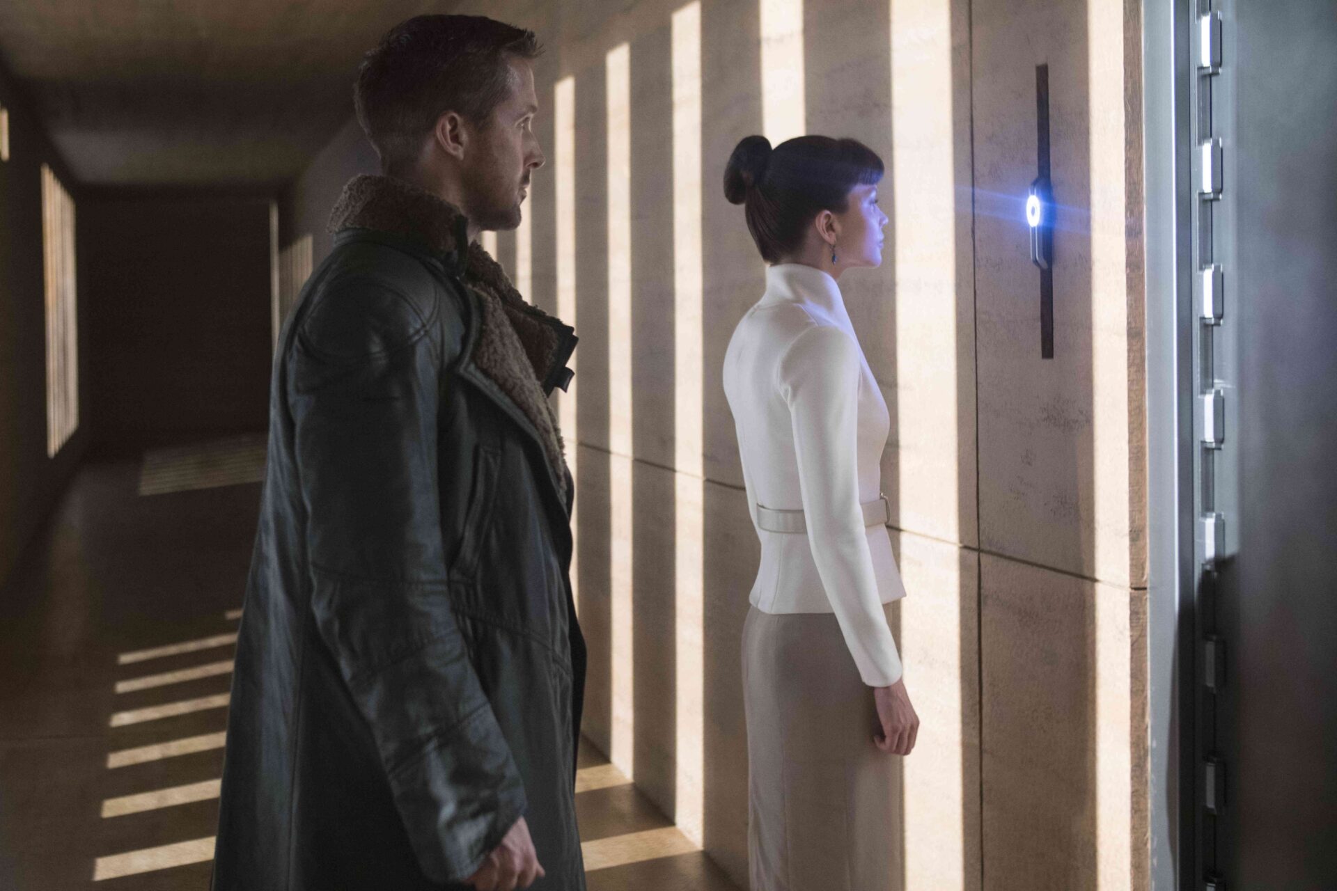 Blade Runner 2049: Das Bild zeigt eine Frau, die vor einer Wand steht und ihr Auge abscannen lässt. Hinter ihr steht ein Mann, der wartet