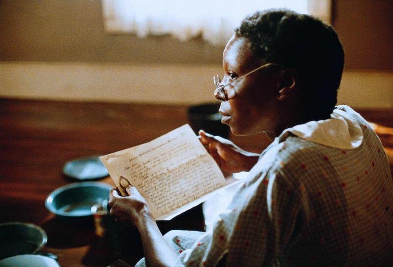 Das Bild zeigt eine Frau, die eine Brille trägt und gerade einen mit Hand geschriebenen Brief liest. Vor ihr ist blaues Geschirr zu sehen