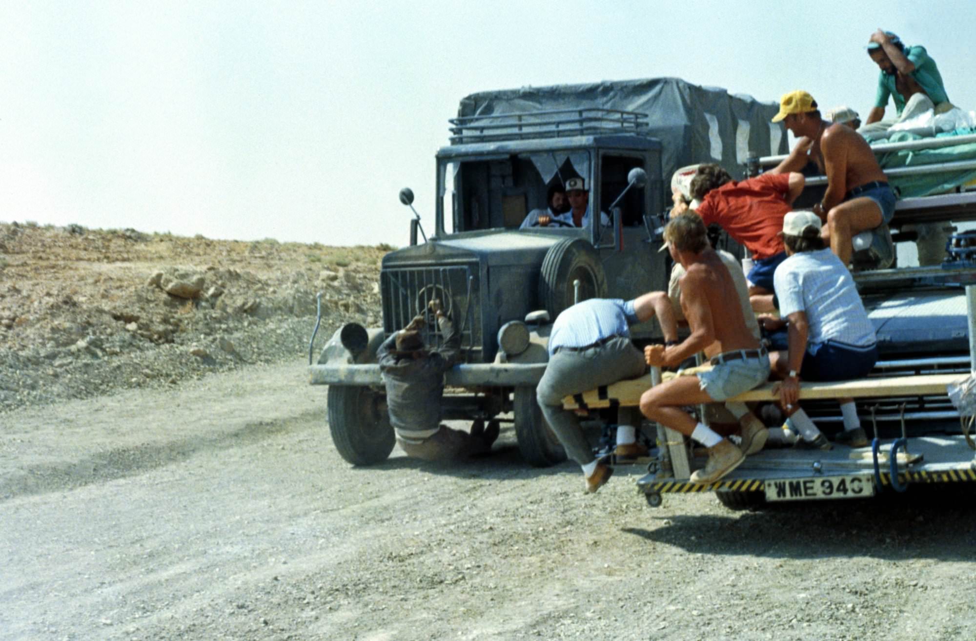 Die besten Action-Filme mit spektakulären Stunts: Das Bild zeigt ein Auto, an dem vorne ein Mann hängt und über die Straße geschleift wird. Daneben ist ein weiteres Auto, auf dem eine Gruppe Menschen sitzt