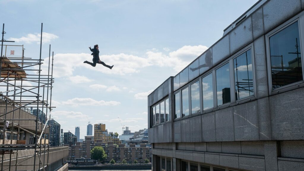 Das Bild zeigt Tom Cruise der gerade von einem Gerüst an eine Häuserwand springt