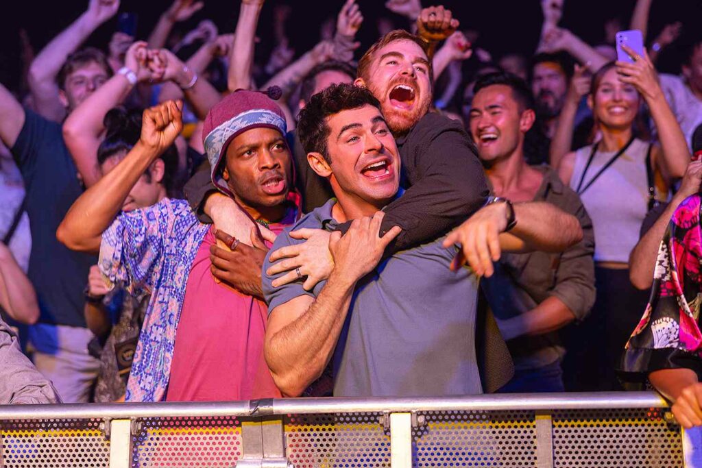 Ricky Stanicky: Das Bild zeigt drei Männer in einer Menschenmenge in einem Konzert, die sich umarmen und lachen