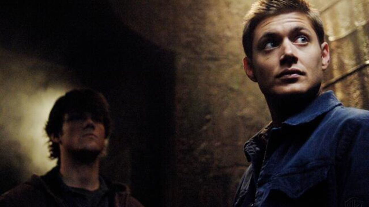 Supernatural Staffel 1: Das Bild zeigt zwei Männer. Einer ist im Hintergrund nur schemenhaft erkennbar, während der andere im Vordergrund an der Wand lehnt