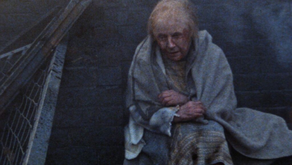 Threads: Auf dem Bild ist eine Frau, die an einer Mauer sitzt, kaum noch Haare auf dem Kopf hat und im Gesicht blutet. Sie hat sich in dünne Decken gewickelt