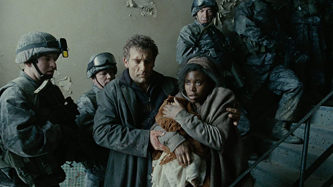 Children of Men: Auf dem Bild ist ein Mann und eine Frau, die in einem Treppenhaus stehen. Die Frau hält etwas in ihren Armen, der Mann stützt sie. Hinter ihnen sind Soldaten zu sehen