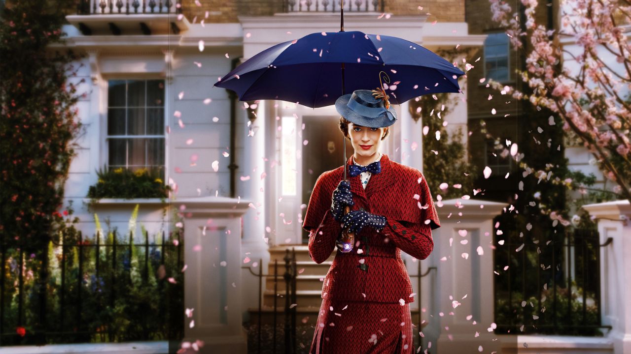 Mary Poppins’ Rückkehr: Auf dem Bild ist eine Frau zu sehen im roten Kostüm. Sie trägt einen blauen Hut und einen blauen Schirm. Die Frau steht vor einem Haus