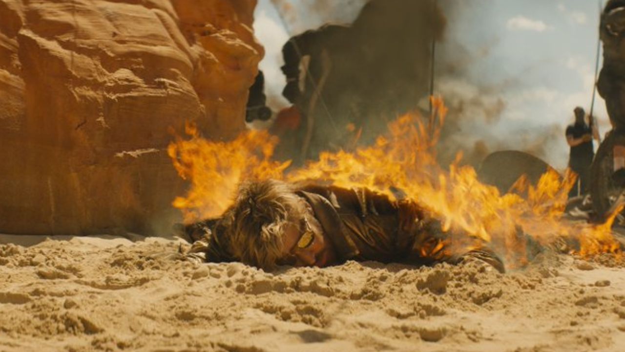 Das Bild zeigt einen Mann, der im Sand liegt und brennt