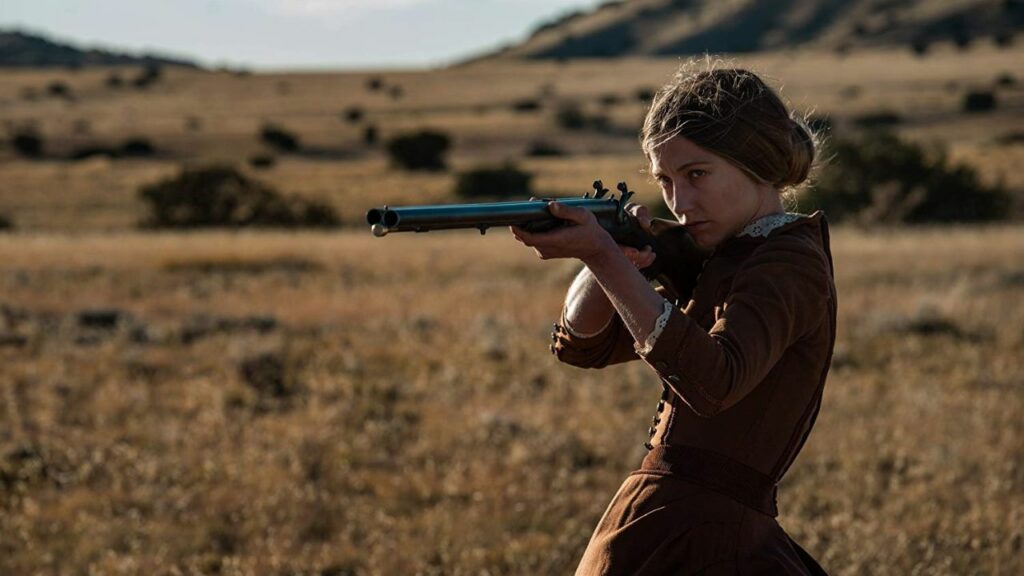 Top 5 Western Filme: Auf dem Bild ist eine Frau in der Prärie zu sehen, die eine Schrotflinte vor sich hält und zielt
