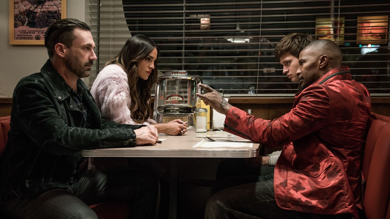 Das Bild zeigt vier Menschen an einem Tisch im Restaurant: Auf der linken Seite sitzen ein Mann in Lederjacke, am Fenster eine junge Frau in rosa Plüschjacke. Rechts sind ein Mann mit auffällig roter Jacke, daneben ein jüngerer Mann