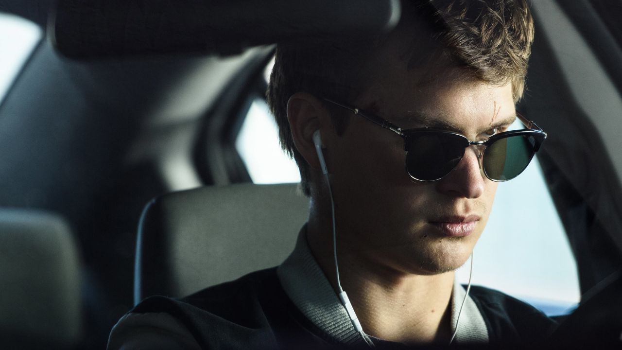 Auf dem Bild sitzt ein junger Mann am Steuer eines Auto, mit Sonnenbrille und Kopfhörern