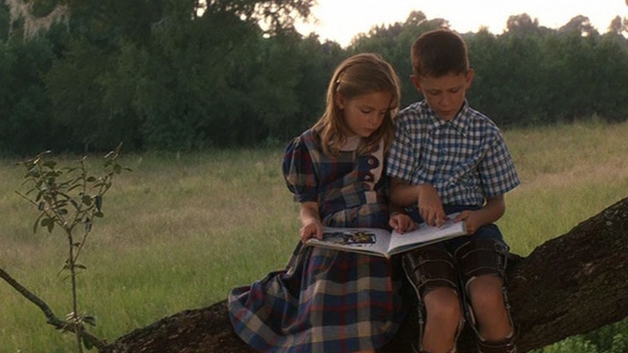 Forrest Gump: Das Bild zeigt einen Jungen und ein Mädchen, die auf einem Baumstamm sitzen und ein Buch lesen