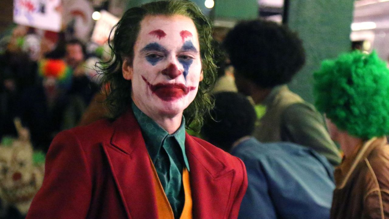 Joker: Das Bild zeigt einen Clown, der verbittert drein blickt. Im Hintergrund ist eine Menschenmenge zu sehen