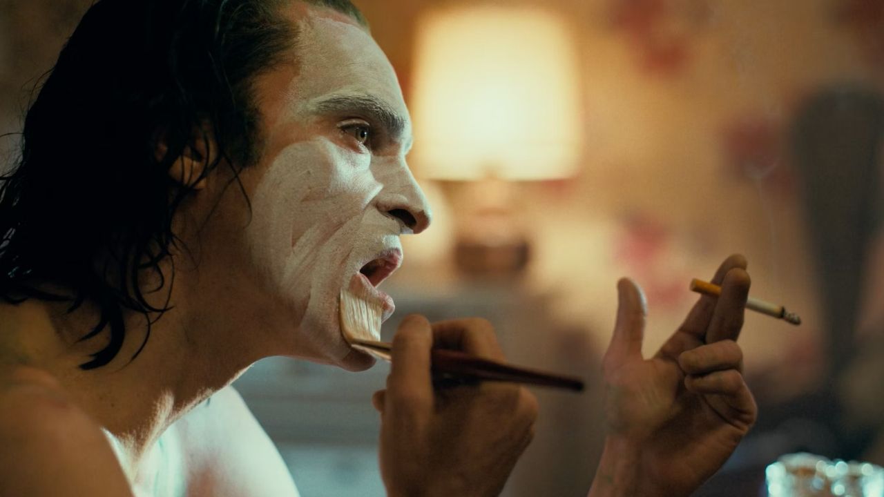 Joker: Das Bild zeigt einen Mann von der Seite, der eine Zigarette in der Hand hat und sich mit einem Pinsel das Gesicht weiß anmalt