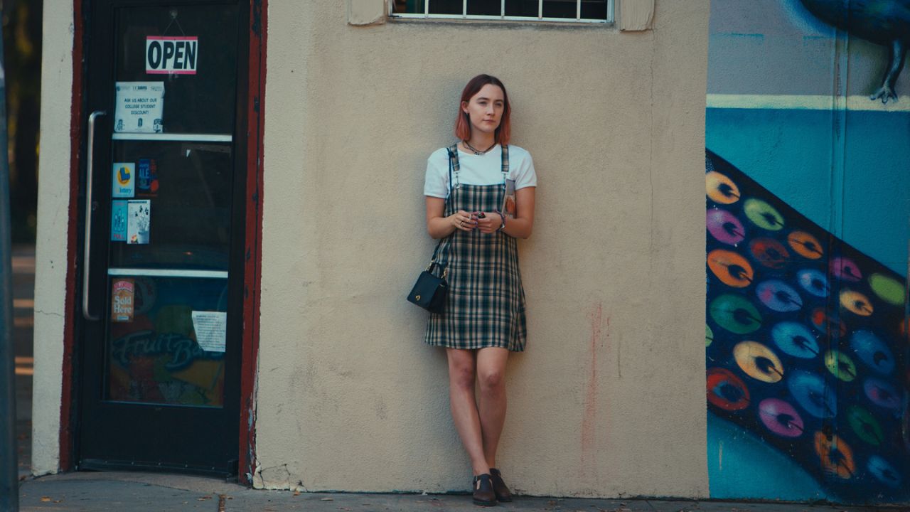 Das Bild zeigt eine junge Frau, die an einer Hauswand eines Ladens lehnt