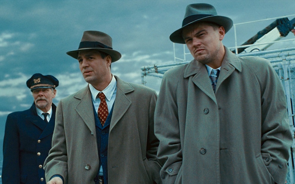 Plot-Twist: Das Bild zeigt drei Männer. Zwei davon tragen Hüte und Trenchcoat. Der dritte Herr ganz links trägt eine Kapitätuniform