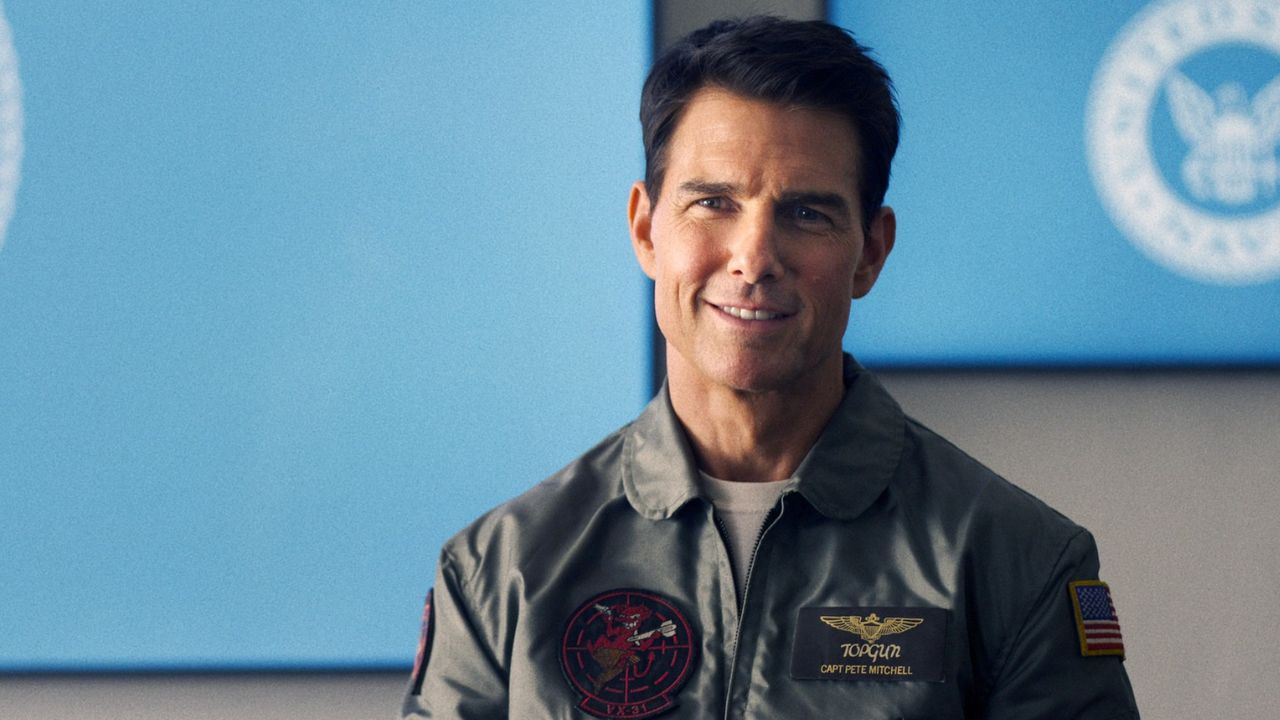 Top Gun: Maverick: Das Bild zeigt einen Mann in Uniform, der vor einem blauen Bildschirm steht und lächelt