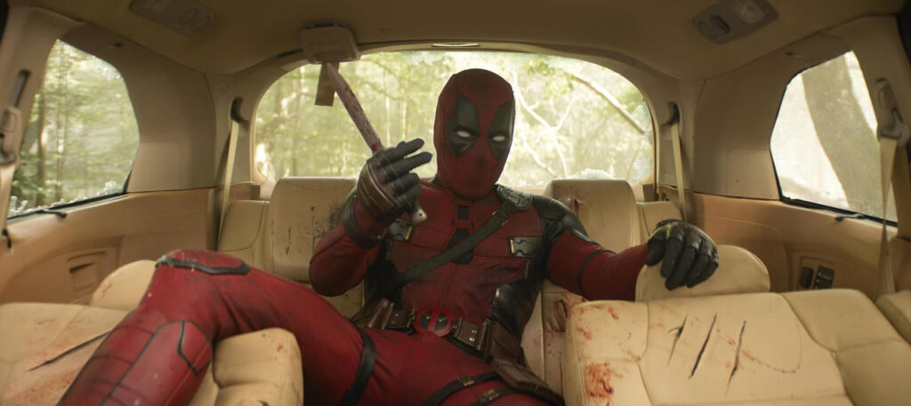 Deadpool and Wolverine: Auf dem Bild ist ein Mann zu sehen, der in einem Auto sitzt. Er trägt ein Superhelden Kostüm und hat eine Maske auf. Außerdem hat er ein Messer in der Hand