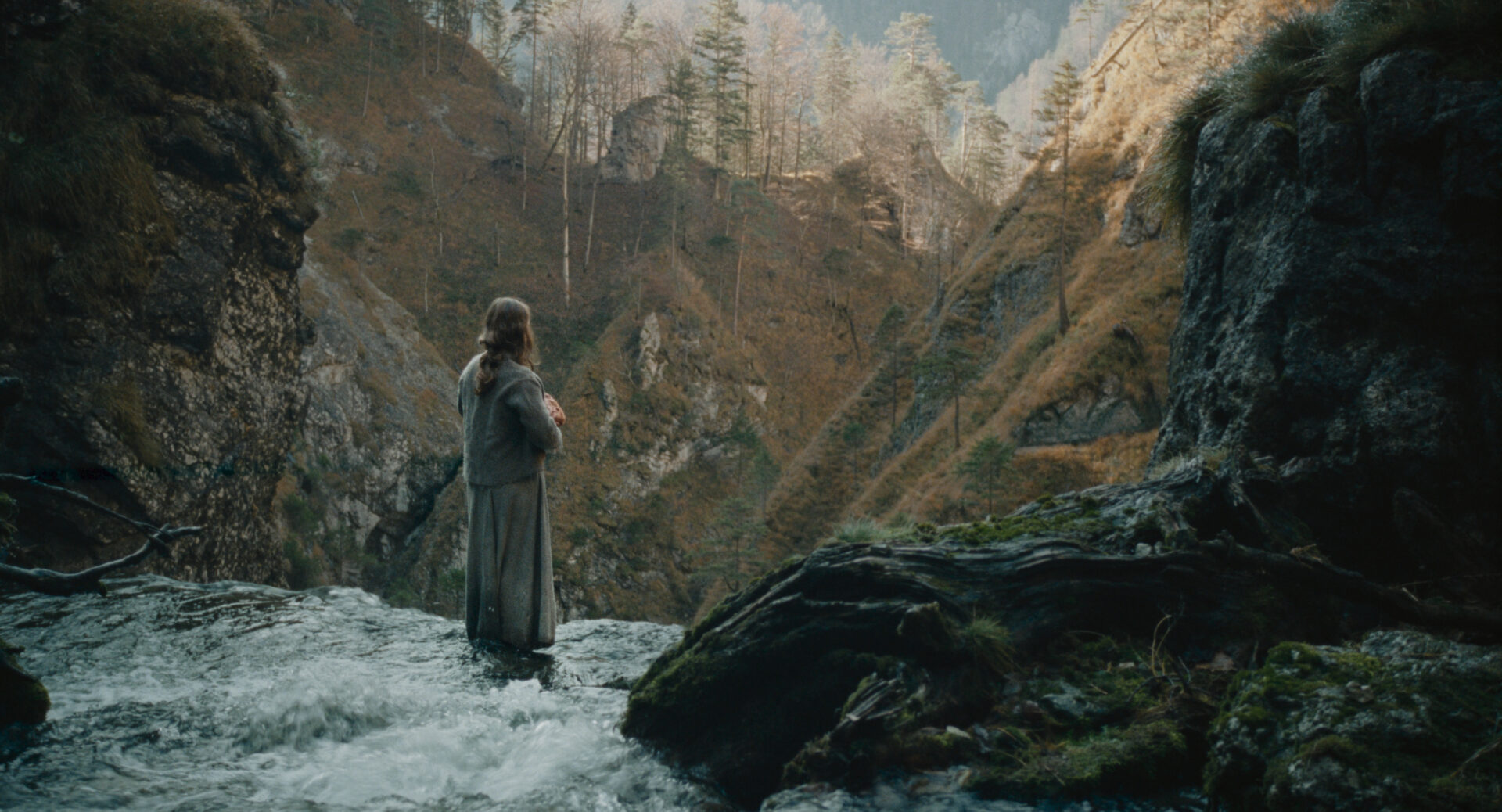 Eine Frau steht an einem Wasserfall. In den Händen hält sie ein Bündel.