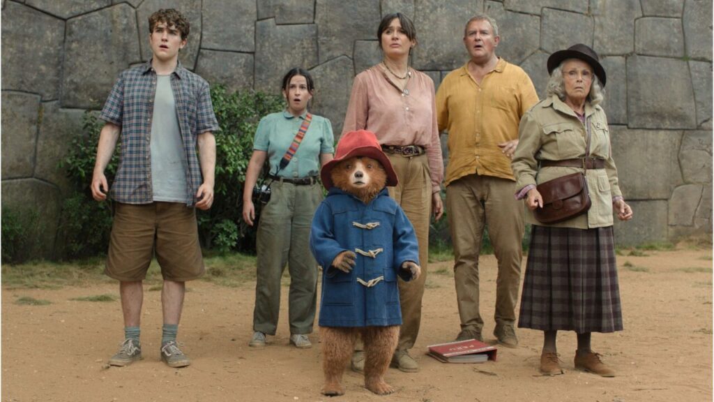 Paddington und Familie Brown schauen erstaunt. Im Hintergrund eine alte Steinmauer.