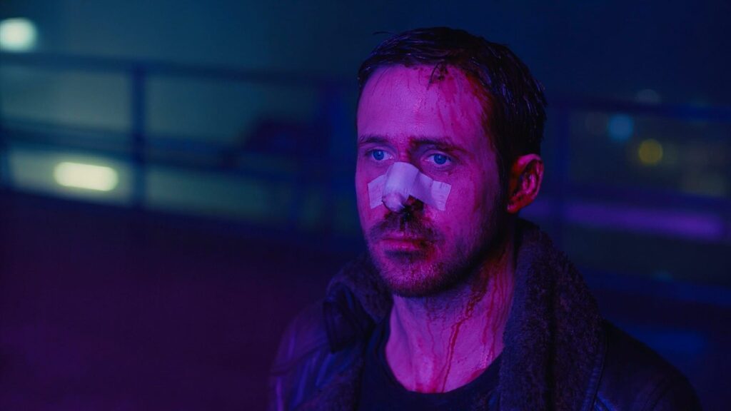 Blade Runner 2049: Das Bild zeigt Officer K in lilafarbenes Neonlicht getaucht. Er blutet im Gesicht und hat ein Pflaster auf seiner Nase. Sein Blick ist traurig