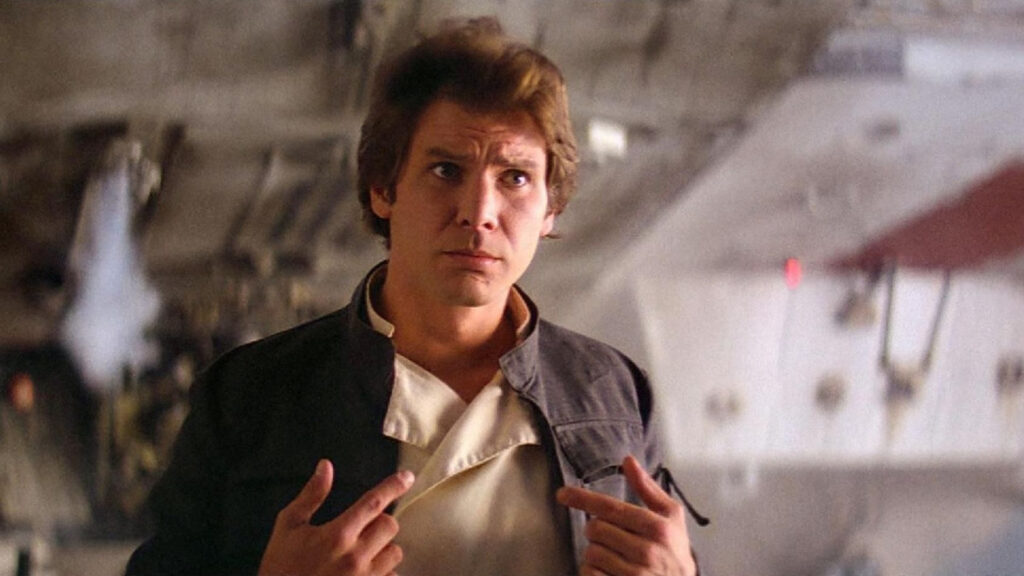 Han Solo trägt eine graue Jacke über einem beigen Hemd und steht im Inneren des Millennium Falken. Er zeigt mit beiden Händen auf sich selbst, was eine selbstbewusste Haltung suggeriert. Der Hintergrund besteht aus technischen Geräten und metallischen Strukturen. | Media Monday #720