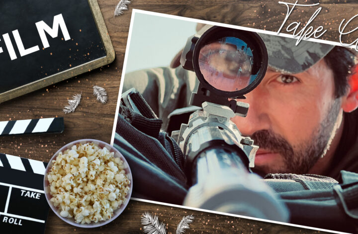 Im Vordergrund ist eine Filmklappe mit beschrifteten Feldern wie „Scene“, „Cut“, „Take“, begleitet von einer Schale Popcorn. Im Hintergrund ist eine Person in Bauchlage zu sehen. Sie trägt eine Kappe und Sonnenbrille und zielt mit einem Gewehr, das mit einem Zielfernrohr ausgestattet ist. Im Vordergrund befindet sich eine schwarze Tasche oder ein Etui. Der Hintergrund deutet auf eine Outdoor-Umgebung hin, möglicherweise bei einer Schießübung oder einem Training. Am oberen rechten Rand stehen die Wörter „Take Cover“ in geschwungener Schrift. Die Szene kombiniert klassische Elemente des Filmemachens und Kinogenusses.