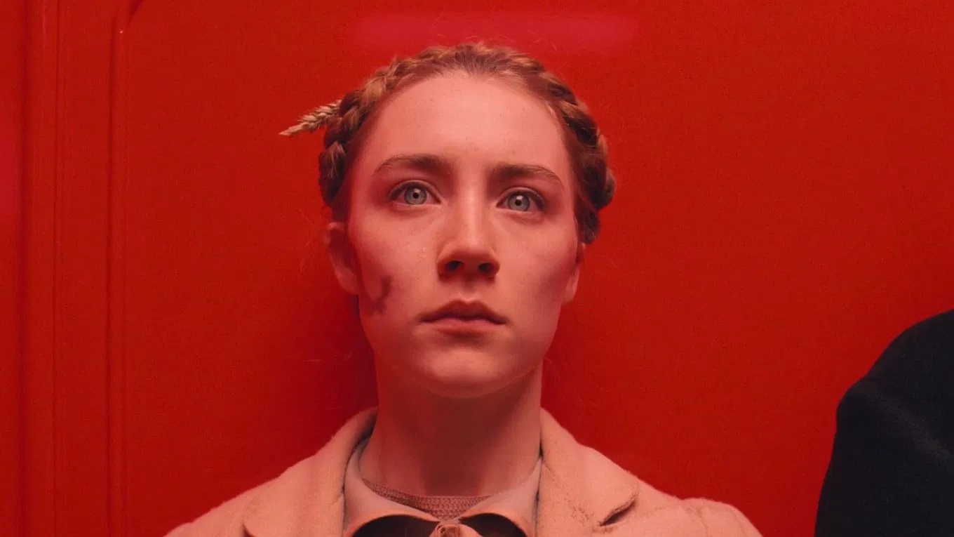 Das Bild zeigt eine junge Frau mit starrem Blick vor einem roten Hintergrund | Die 5 besten Regieführenden des 21. Jahrhunderts