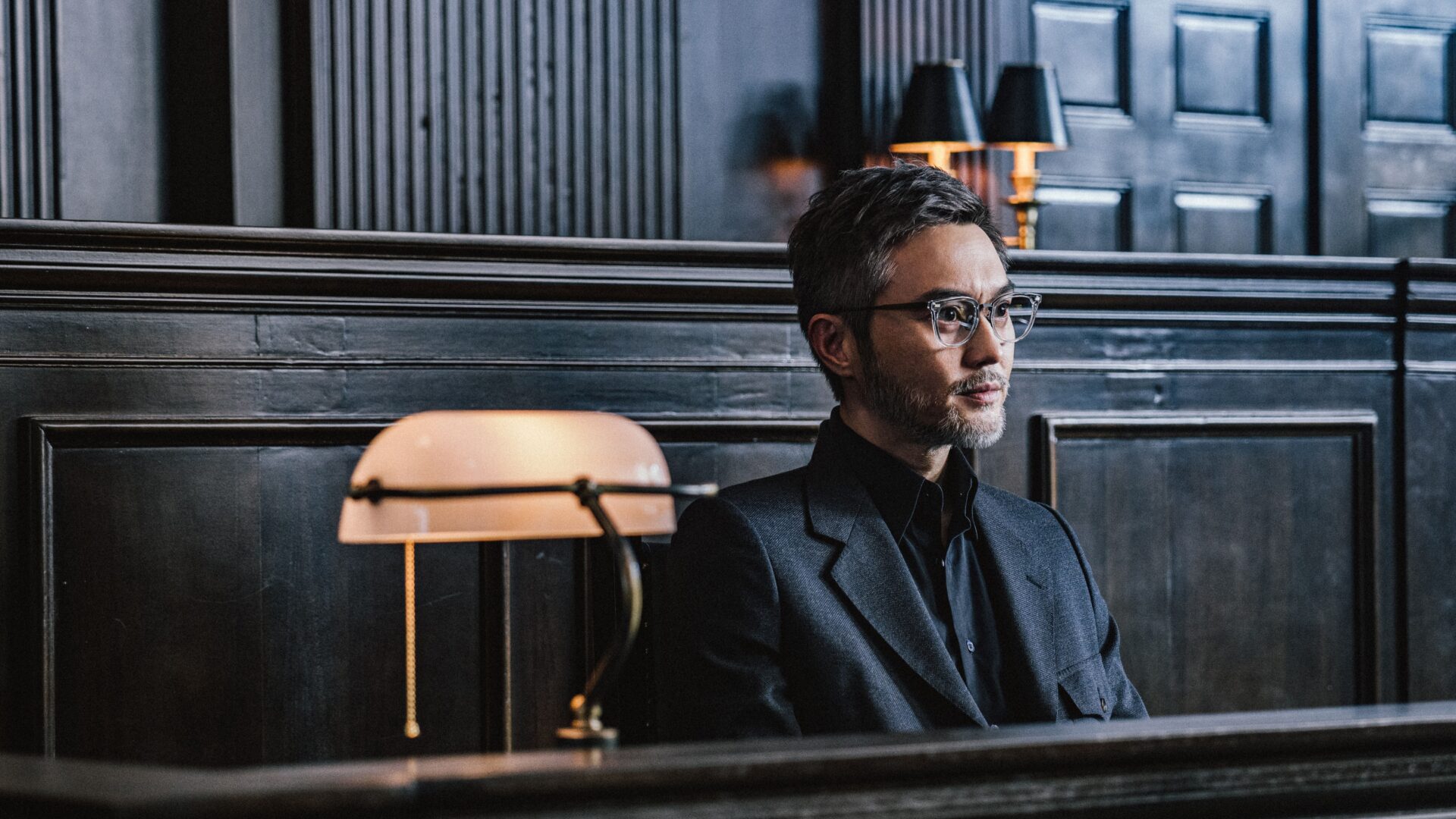 Julian Cheung sitzt im Film "The Prosecutor" in einem schwarzen Anzug auf einer Bank.