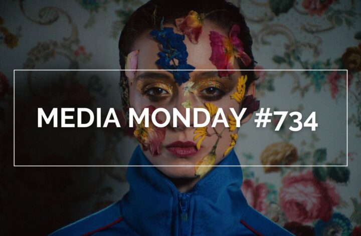 Eine Person in einer blauen Jacke mit roten Akzenten steht vor einer Tapete mit floralem Muster. Quer über das Bild ist der Text „MEDIA MONDAY #734“ eingeblendet.