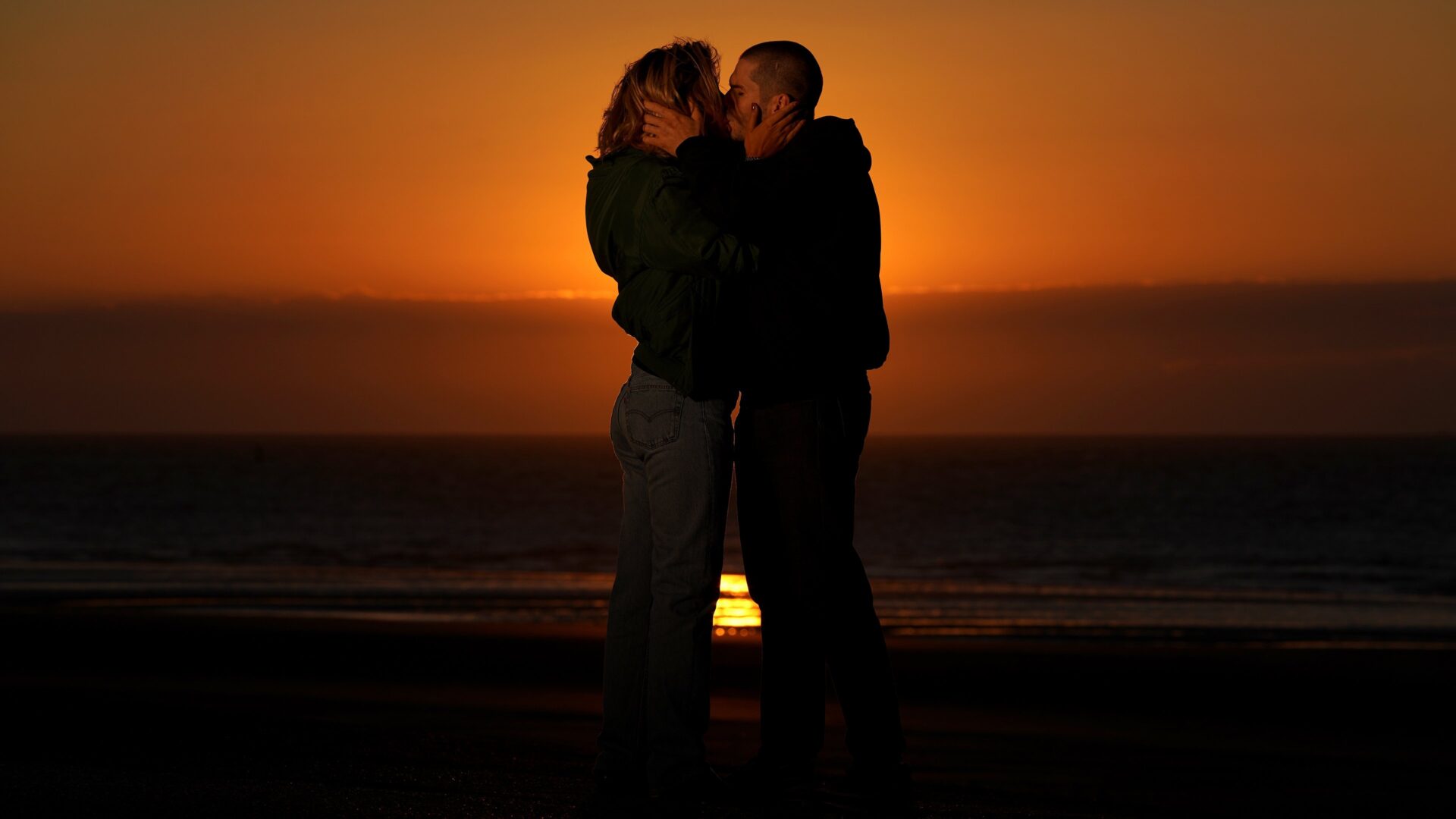 Zwei Personen küssen sich, im Hintergrund ein Sonnenuntergang.